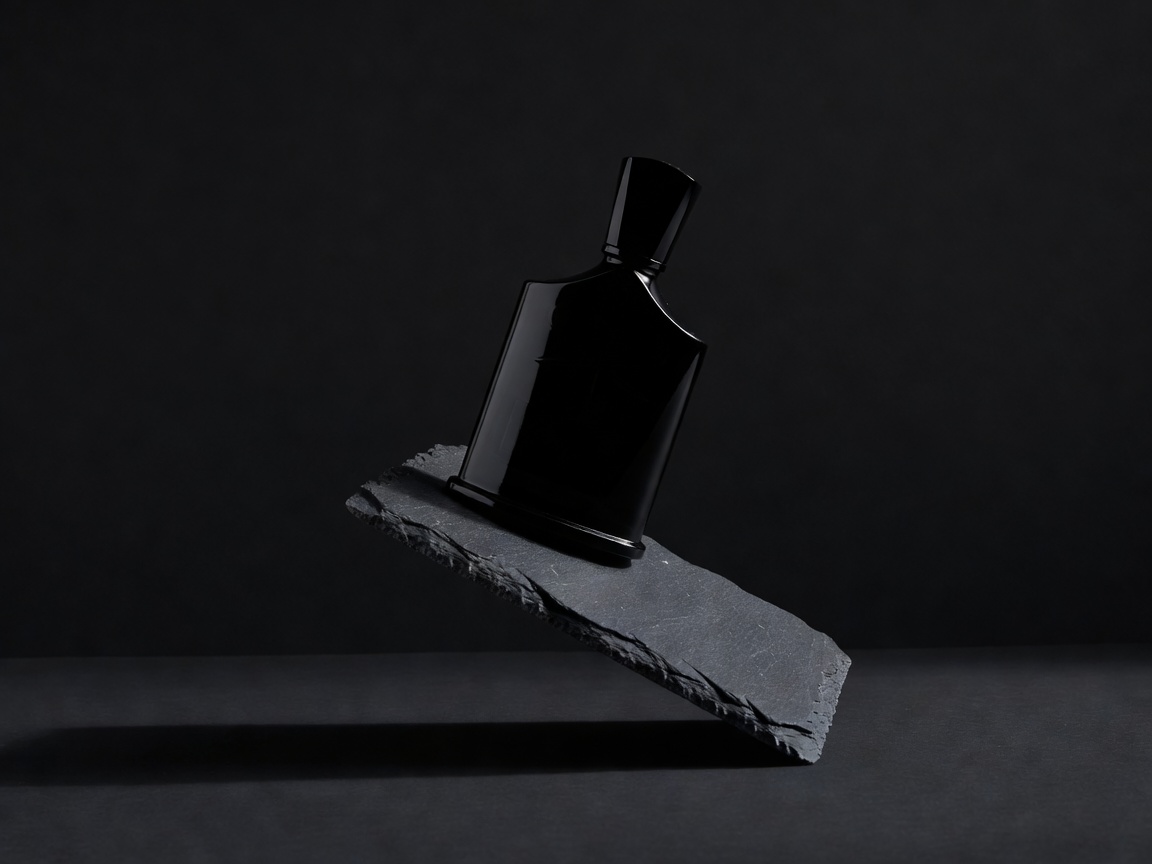 Creed Aventus black glass perfume bottle balanced on an angled slate block in low studio light